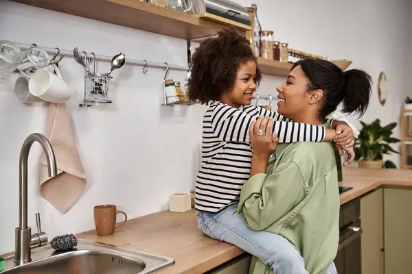 A mother lovingly embraces her little daughter while enjoying morning together in a cozy kitchen. — Stock Photo