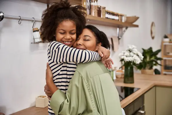 A mother and daughter share a warm hug in their cozy kitchen, celebrating their bond. — Stock Photo