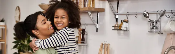A woman lovingly holds her smiling daughter in a warm, welcoming kitchen atmosphere. — Stock Photo
