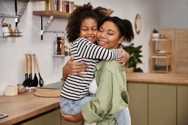 A joyful mother embraces her little daughter in a bright and welcoming kitchen together. — Stock Photo
