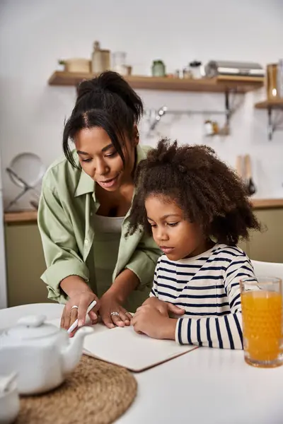 A mother guides her daughter as they draw together at a cheerful kitchen table. — Stock Photo
