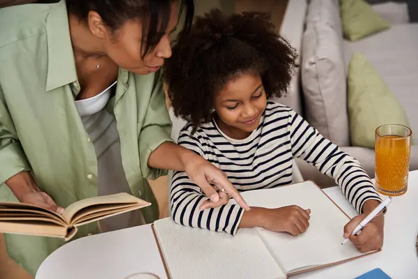 Una madre cariñosa ayuda a su hija a escribir en un cuaderno, disfrutando del tiempo juntos. - foto de stock