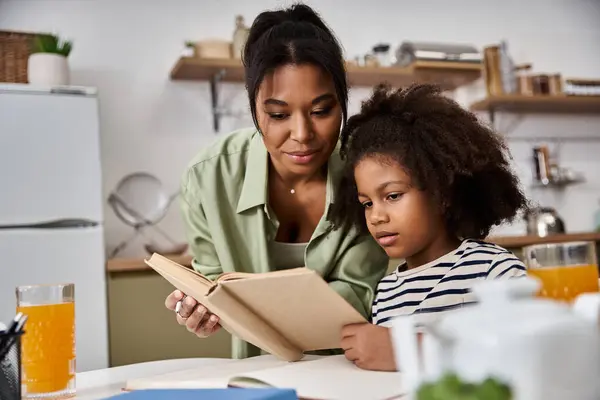 A joyful mother reads with her daughter in their modern kitchen, sharing a special bond. — Stock Photo