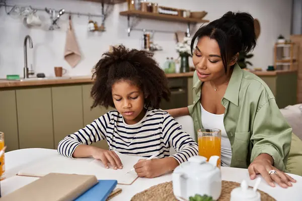 A mother helps her daughter draw at a bright kitchen table, enjoying a cozy afternoon. — Stock Photo