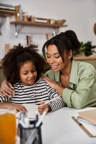 Eine Mutter unterstützt ihre Tochter liebevoll bei einer Aktivität am Küchentisch in einem warmen Ambiente. — Stockfoto