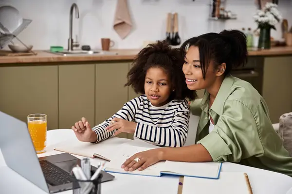 Una madre cariñosa ayuda a su niña con el aprendizaje en línea en su cocina cálida y acogedora. - foto de stock