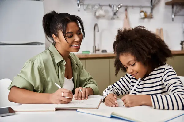 A loving mother helps her daughter with homework at their cozy kitchen table on a bright day. — Stock Photo
