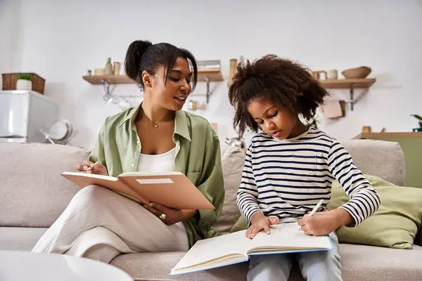 A mother sits beside her daughter, guiding her with schoolwork in a cozy living room. — Stock Photo