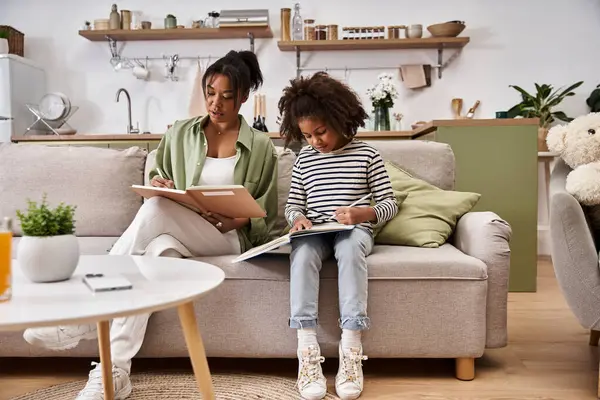 A mother and daughter sit side by side on a sofa, happily working on their art projects. — Stock Photo