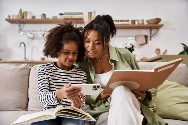 Loving mother and daughter share a joyful moment reading and looking at a device on a comfy couch — Stock Photo