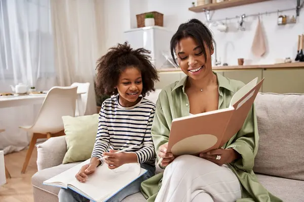 A mother and daughter happily read together on a cozy sofa in their bright living room. — Stock Photo