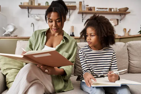 A mother and daughter joyfully explore books together on a cozy couch. — Stock Photo