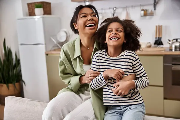 A mother and her daughter are laughing together in a bright kitchen, sharing a loving moment. — Stock Photo