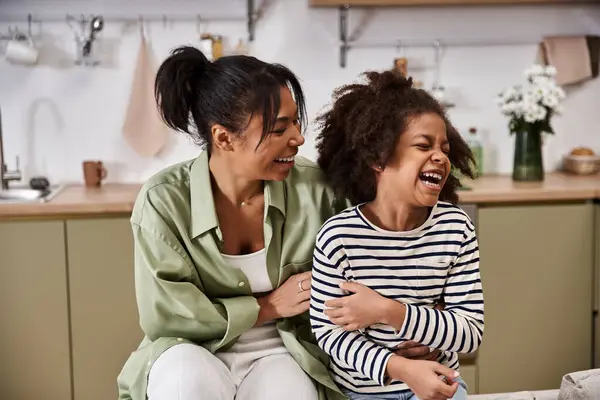 Una madre gioiosa e sua figlia condividono una risata in una cucina luminosa e moderna, creando ricordi. — Foto stock