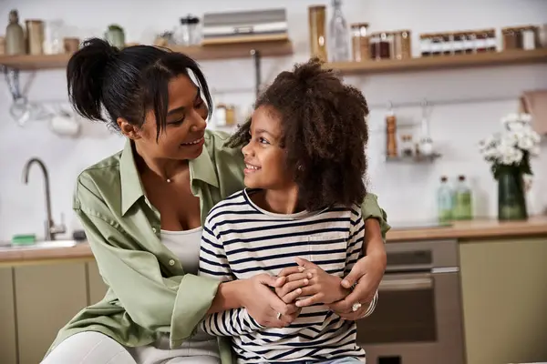 A mother and her daughter share joyful laughter while embracing in their cheerful kitchen. — Stock Photo