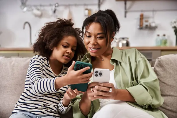 Loving mother and her daughter explore their smartphones together in a cozy living space. — Stock Photo