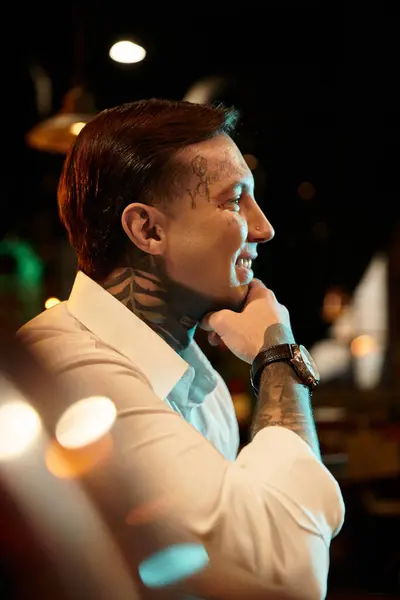 A young man with striking tattoos enjoys a lively evening at a bar, radiating confidence. — Stock Photo