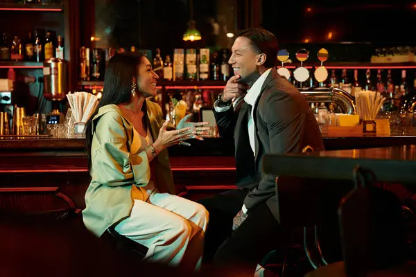 A multicultural couple shares laughter and drinks at a vibrant bar on a night out. — Stock Photo