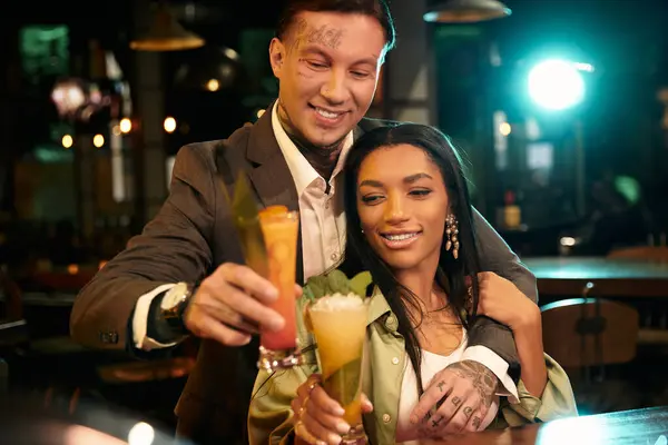 A young couple shares laughter while toasting their colorful cocktails, enjoying their evening. — Stock Photo