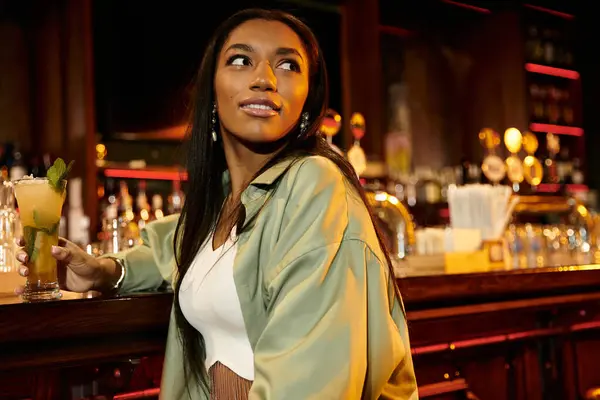 Young woman having a drink in a lively bar, embracing the nightlife atmosphere. — Stock Photo