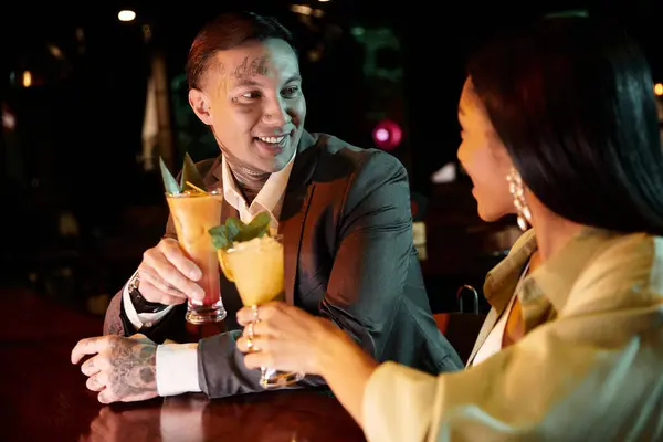 Tattooed man and woman share cocktails and smiles on a lively night out at a bar. — Stock Photo