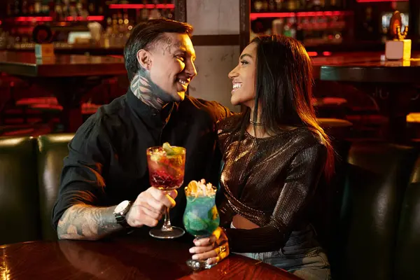Casal tatuado compartilha risos e coquetéis durante uma noite animada em um bar movimentado. — Fotografia de Stock