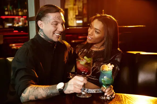 Young couple shares a joyful moment, sipping cocktails in a vibrant bar ambiance. — Stock Photo