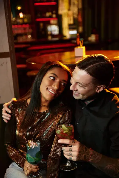 A young couple shares a joyful moment while sipping colorful drinks on a lively night out. — Stock Photo