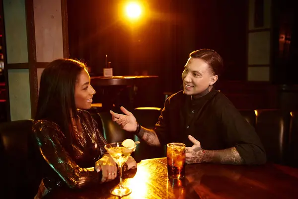 Junges Paar unterhält sich fröhlich, während es an einer lebhaften Bar Cocktails schlürft. — Stockfoto