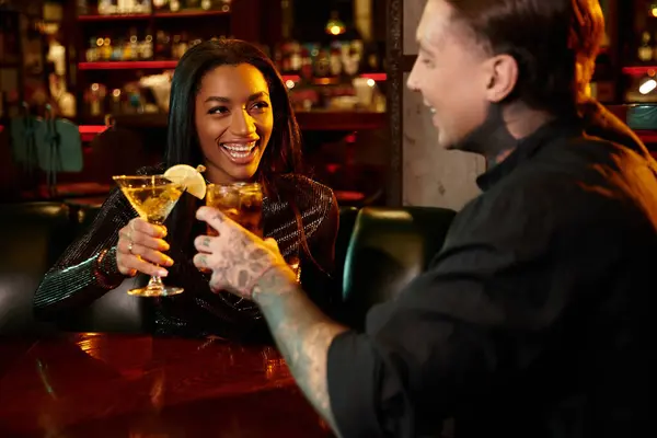 A tattooed couple clinks glasses while on a fun evening out together in a vibrant bar. — Stock Photo