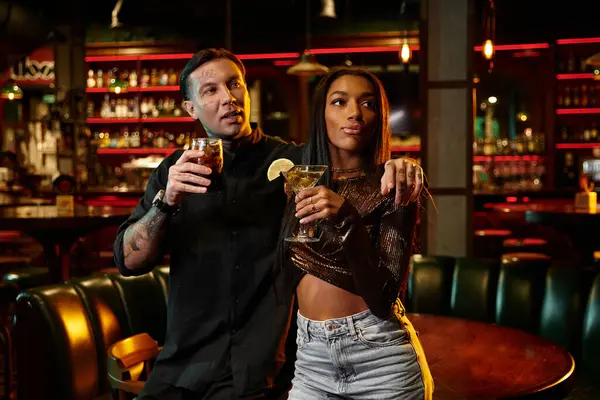 Tätowierte Männer und Frauen teilen sich das Lachen, während sie in einer lebhaften Bar Cocktails schlürfen. — Stockfoto
