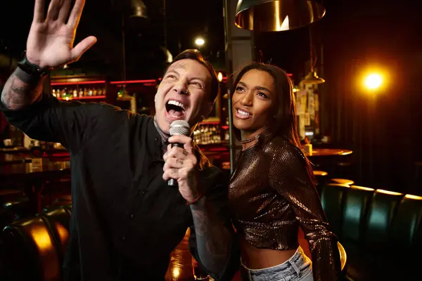 A young couple shares joy while having fun at a bar, singing together under vibrant lights. — Stock Photo