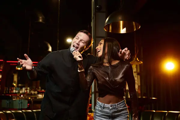 Giovane coppia ride e canta insieme, abbracciando il divertimento di una serata karaoke fuori. — Foto stock