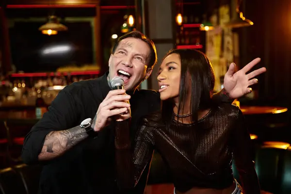 Una giovane coppia multiculturale canta gioiosamente insieme in una vivace serata fuori in un bar. — Foto stock