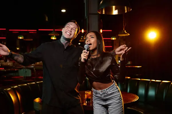 A young couple with tattoos shares a fun moment singing at a lively bar on a night out. — Stock Photo