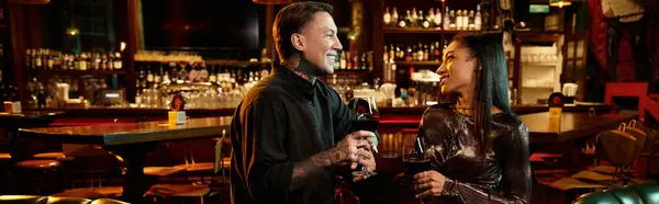 Tattooed man and woman share a romantic night out, holding glasses of wine in a lively bar setting. — Stock Photo