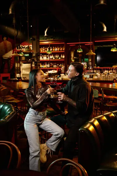 A beautiful multicultural couple share laughter and drinks during their night out at the bar. — Stock Photo