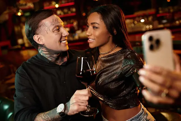 Tattooed man and woman share an intimate moment while enjoying drinks at a lively bar. — Stock Photo