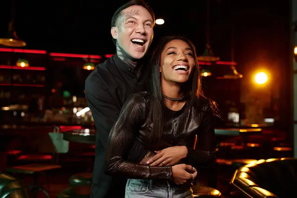A tattooed man and woman share laughter and connection during their evening date at a lively bar. — Stock Photo