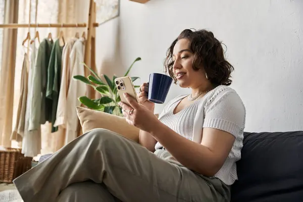 Entspannt nippt eine Frau in ihrer stilvollen Wohnung am Kaffee, während sie in ihrem Smartphone surft. — Stockfoto