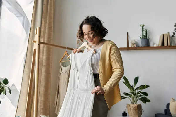 A young woman with curly hair happily checks out a dress in her lively living space. — Stock Photo