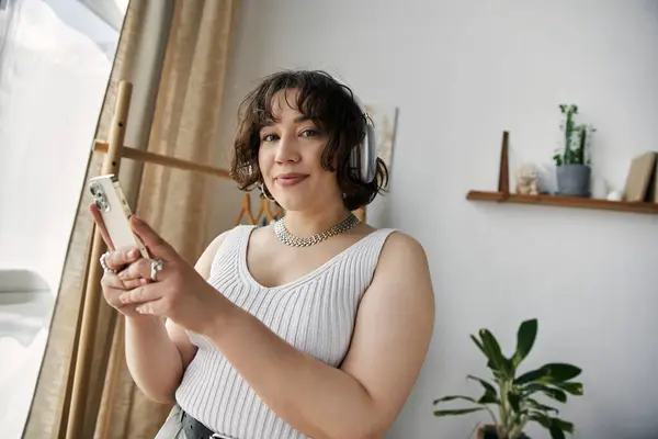 Curly-haired woman engages with her phone, radiating happiness in a modern, sunlit space. — Stock Photo