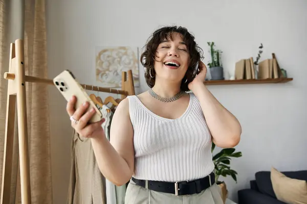 Curly-haired woman enjoys music in her stylish apartment, radiating happiness and confidence. — Stock Photo