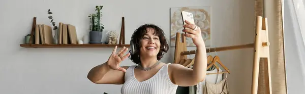 A young woman with curly hair happily engages with her device in a modern living space, banner — Stock Photo