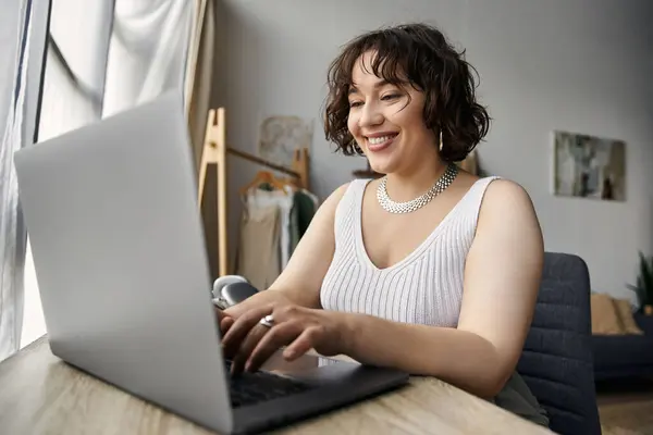 Young woman with curly hair types on her laptop, embracing a cozy, stylish atmosphere. — Stock Photo