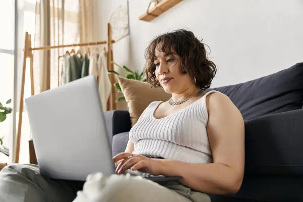 Young woman with curly hair relaxes while working on her laptop in a beautifully designed apartment. — Stock Photo