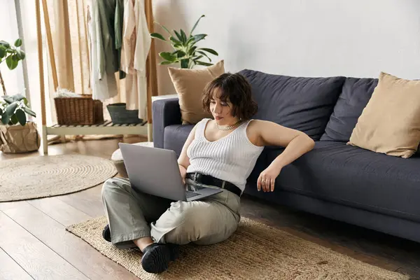 Dans un appartement moderne et serein, une jeune femme aux cheveux bouclés se détend en travaillant sur son ordinateur portable. — Photo de stock