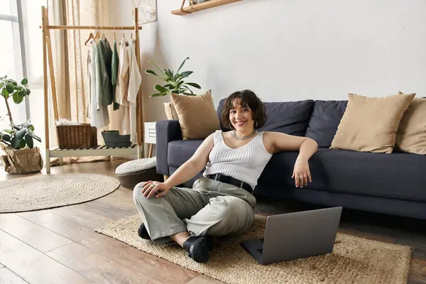 A young woman with curly hair relaxes on the floor of her stylish apartment, radiating joy. — Stock Photo