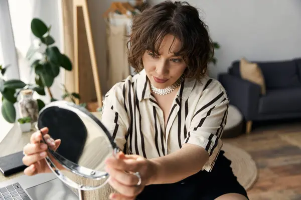 A young woman with curly hair admires her reflection, enjoying a moment of self-care in her home. — Stock Photo
