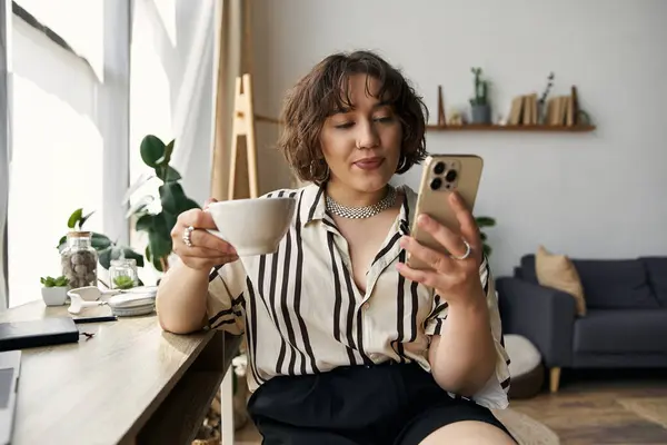 A young woman with curly hair relaxes in her apartment, sipping coffee and using her phone. — Stock Photo